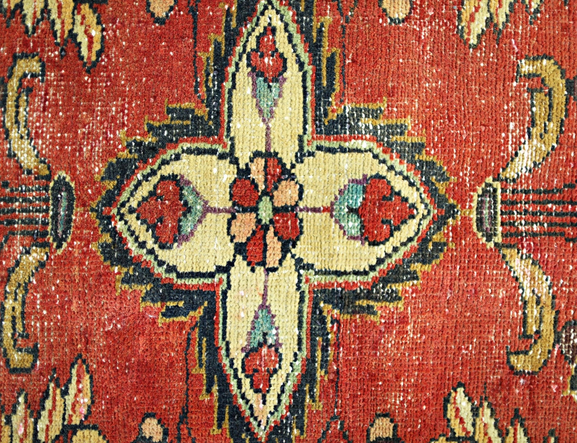 A close-up of a vintage Persian rug featuring a central floral medallion on a red background.