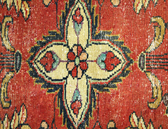 A close-up of a vintage Persian rug featuring a central floral medallion on a red background.