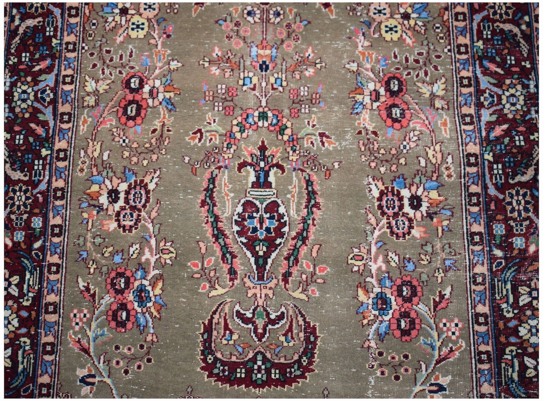 A vintage handwoven Persian rug featuring a central floral vase motif on a muted olive background.