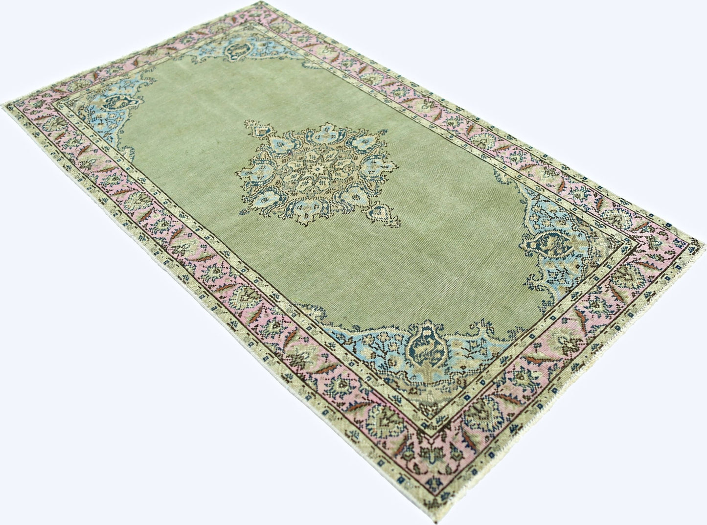 A vintage handmade Persian rug featuring a sage green field with pink and blue floral accents.