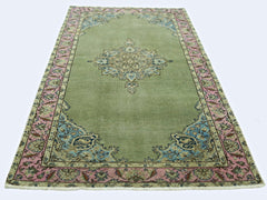 A vintage handmade Persian rug featuring a central floral medallion on a sage green field.