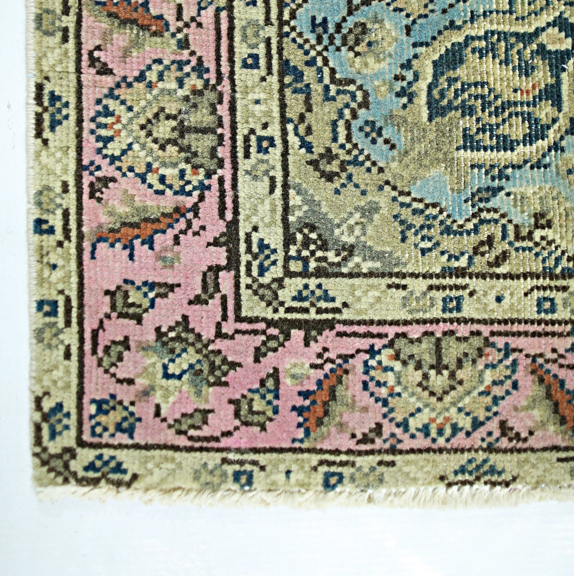 A vintage handmade Persian rug featuring a pink border and intricate blue and beige patterns.