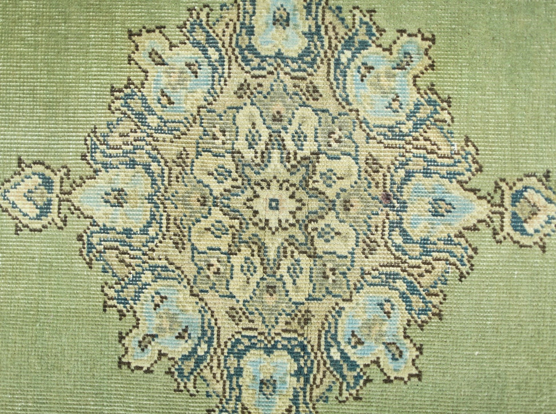 A vintage Persian rug featuring a detailed blue and beige floral medallion on a sage green field.
