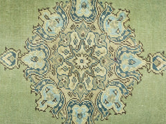 A vintage Persian rug featuring a detailed blue and beige floral medallion on a sage green field.