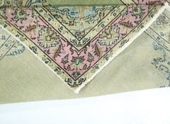 A corner of a vintage handmade Persian rug with a pink floral border and green wool pile.