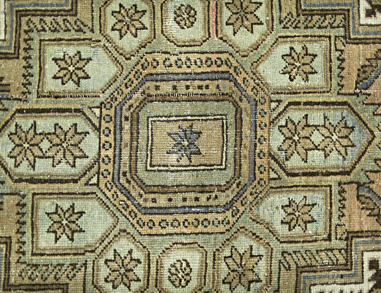 A vintage Persian rug featuring a geometric pattern of octagons and star motifs in muted tones.