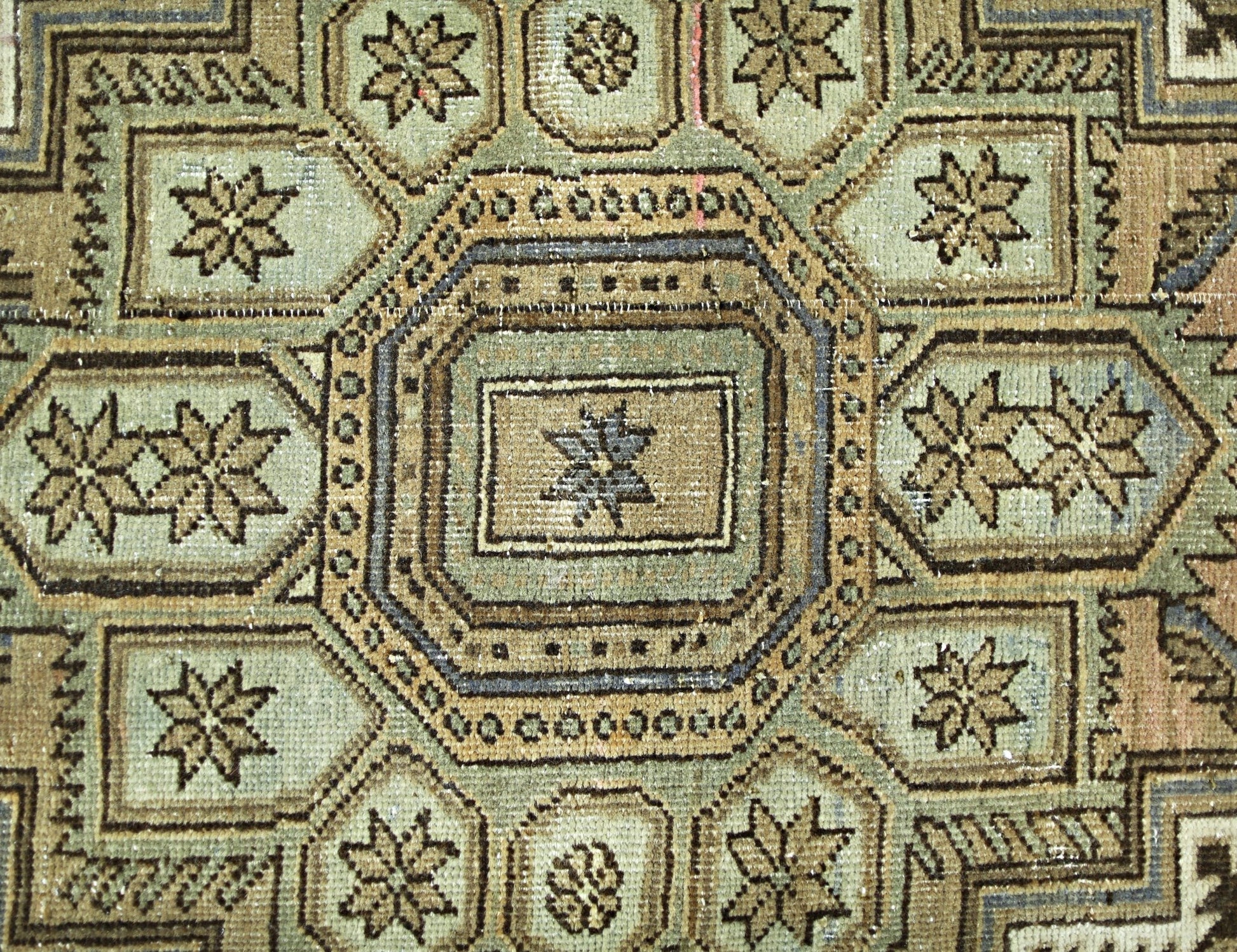 A vintage Persian rug featuring a geometric pattern of octagons and star motifs in muted tones.