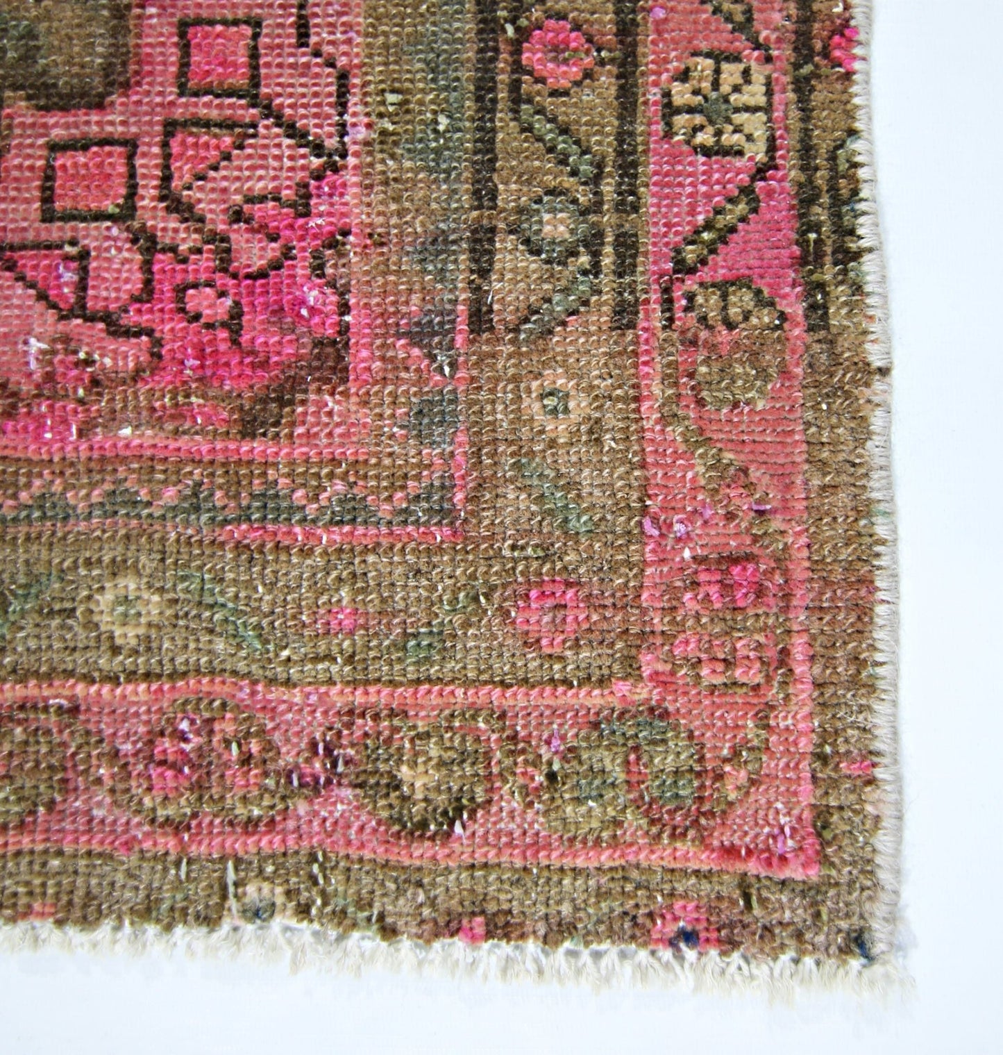 A close-up of a vintage handmade Persian rug featuring intricate geometric patterns in pink and brown.