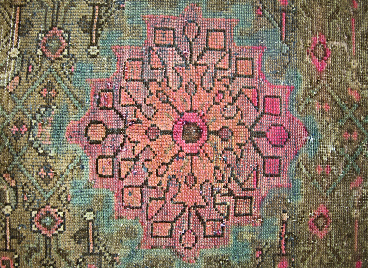 A vintage handmade Persian rug featuring a central pink floral medallion on a brown background.