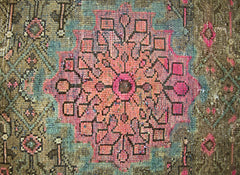 A vintage handmade Persian rug featuring a central pink floral medallion on a brown background.