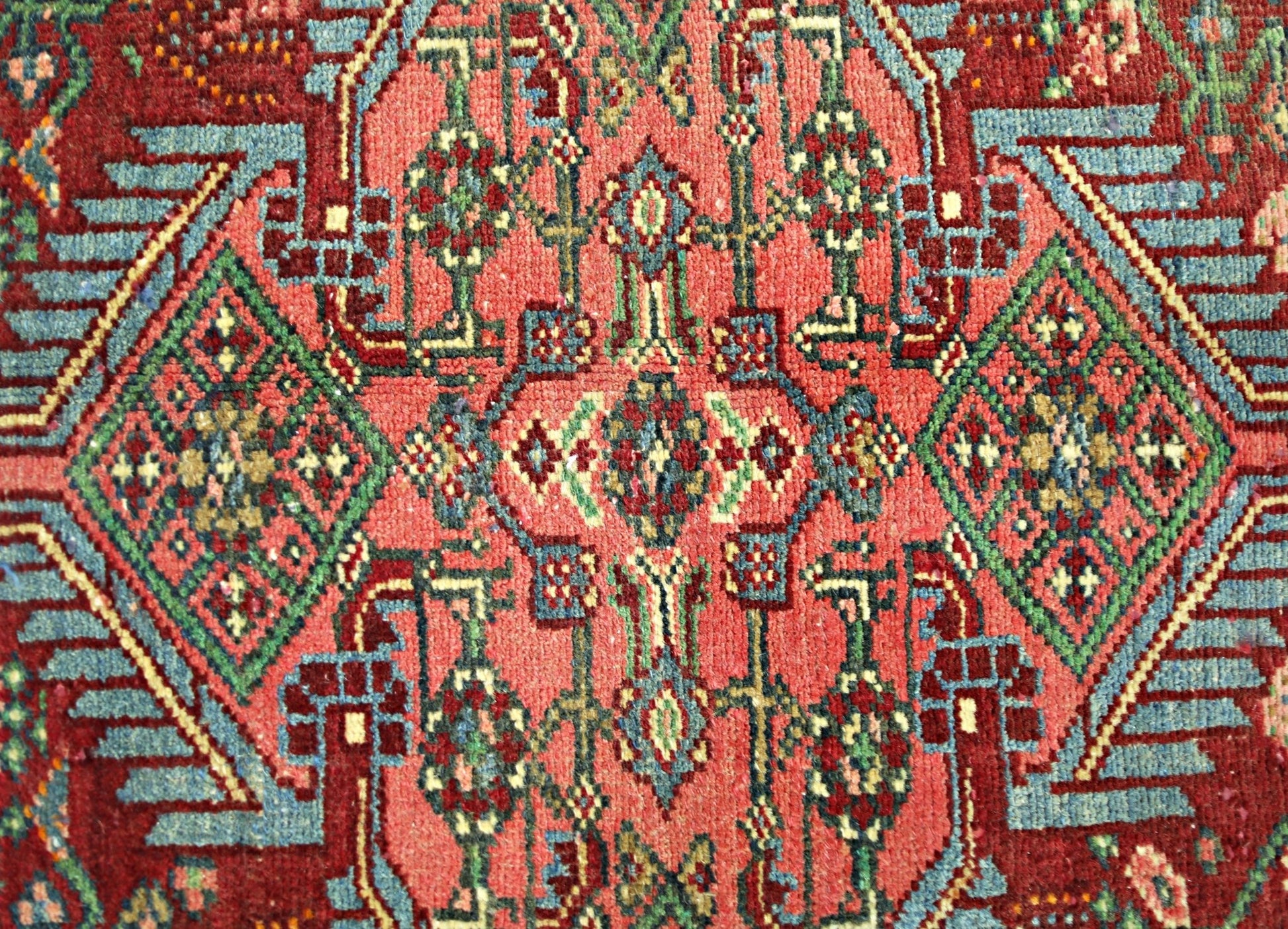 A vintage handmade Persian rug featuring intricate geometric patterns in red, blue, and green.