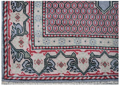 A vintage handwoven Persian rug featuring a geometric red and grey pattern with a floral border.