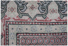 A close-up of a vintage Persian rug featuring intricate geometric patterns in pink, green, and black.