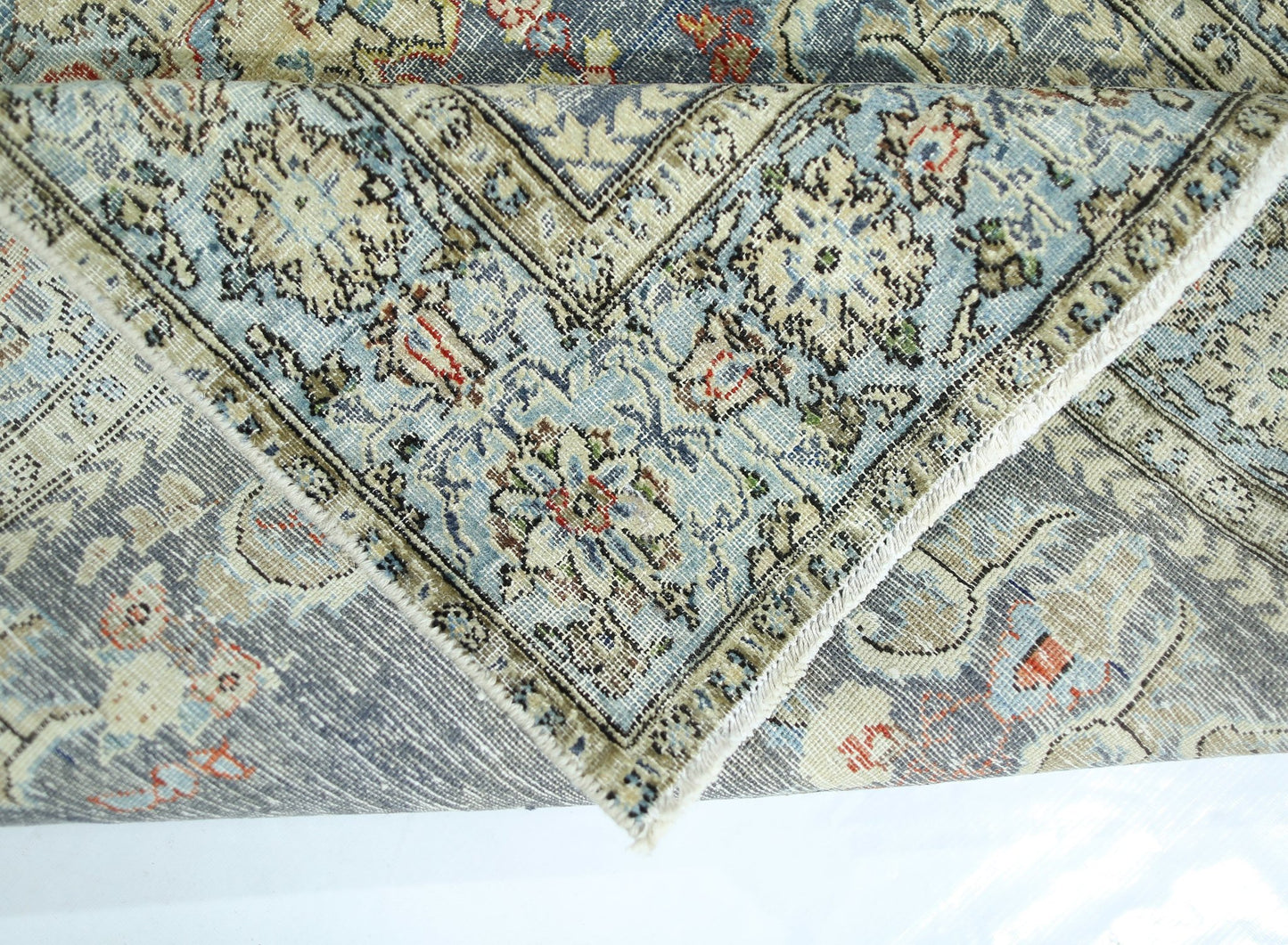 A folded vintage Persian rug featuring intricate floral patterns in blue, cream, and red tones.