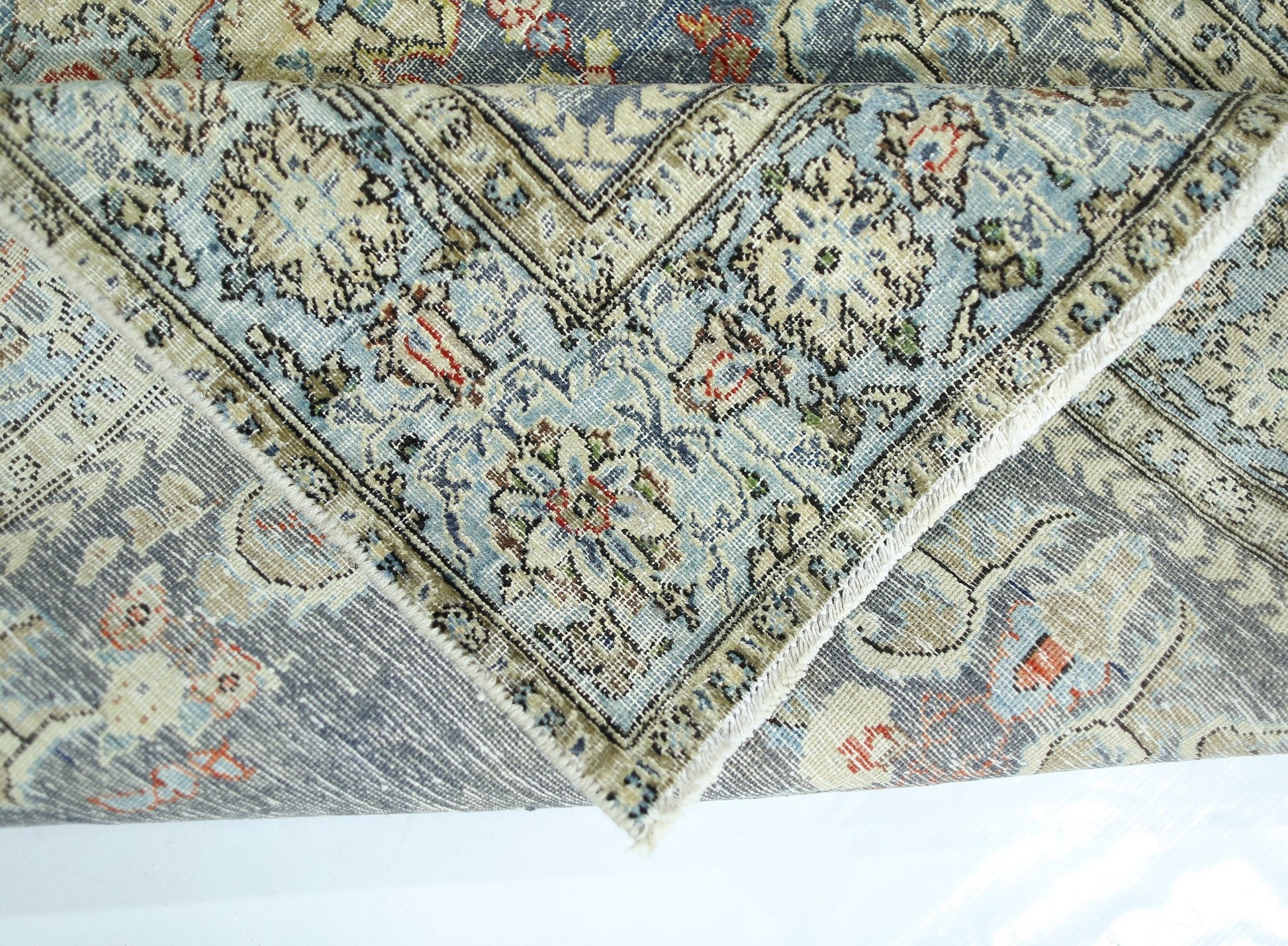 A folded vintage Persian rug featuring intricate floral patterns in blue, cream, and red tones.