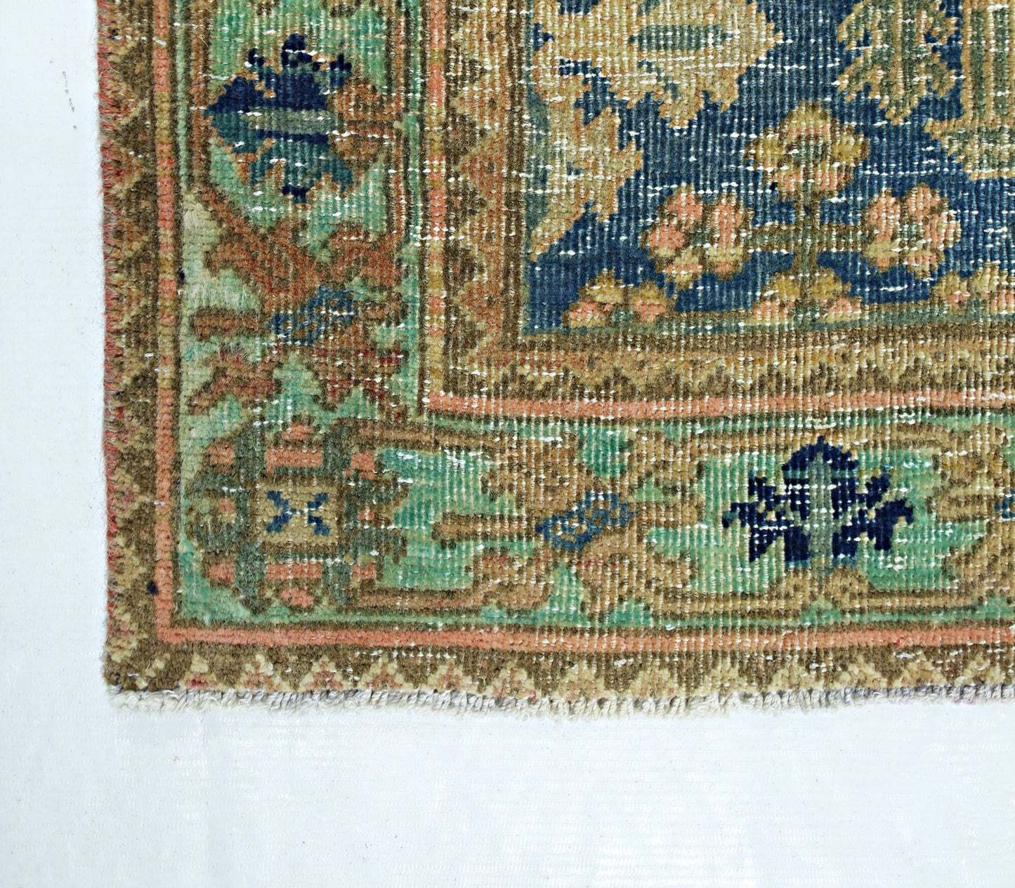 A corner view of a vintage handmade Persian rug featuring intricate floral patterns in blue and green.