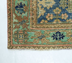 A corner view of a vintage handmade Persian rug featuring intricate floral patterns in blue and green.