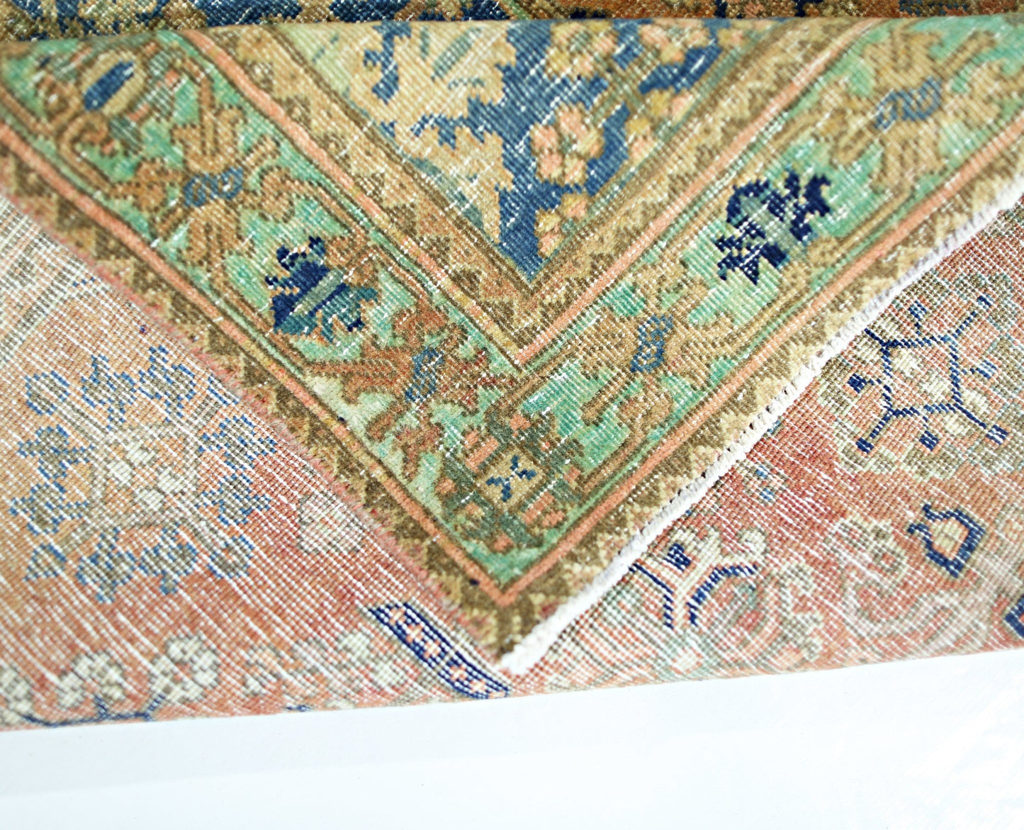 A folded vintage Persian rug featuring intricate floral patterns in blue, green, and orange tones.