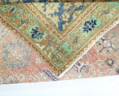 A folded vintage Persian rug featuring intricate floral patterns in blue, green, and orange tones.