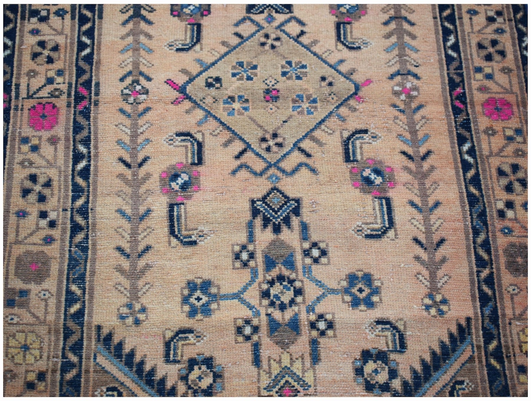 A handwoven vintage Persian rug featuring geometric patterns in blue, pink, and tan wool.