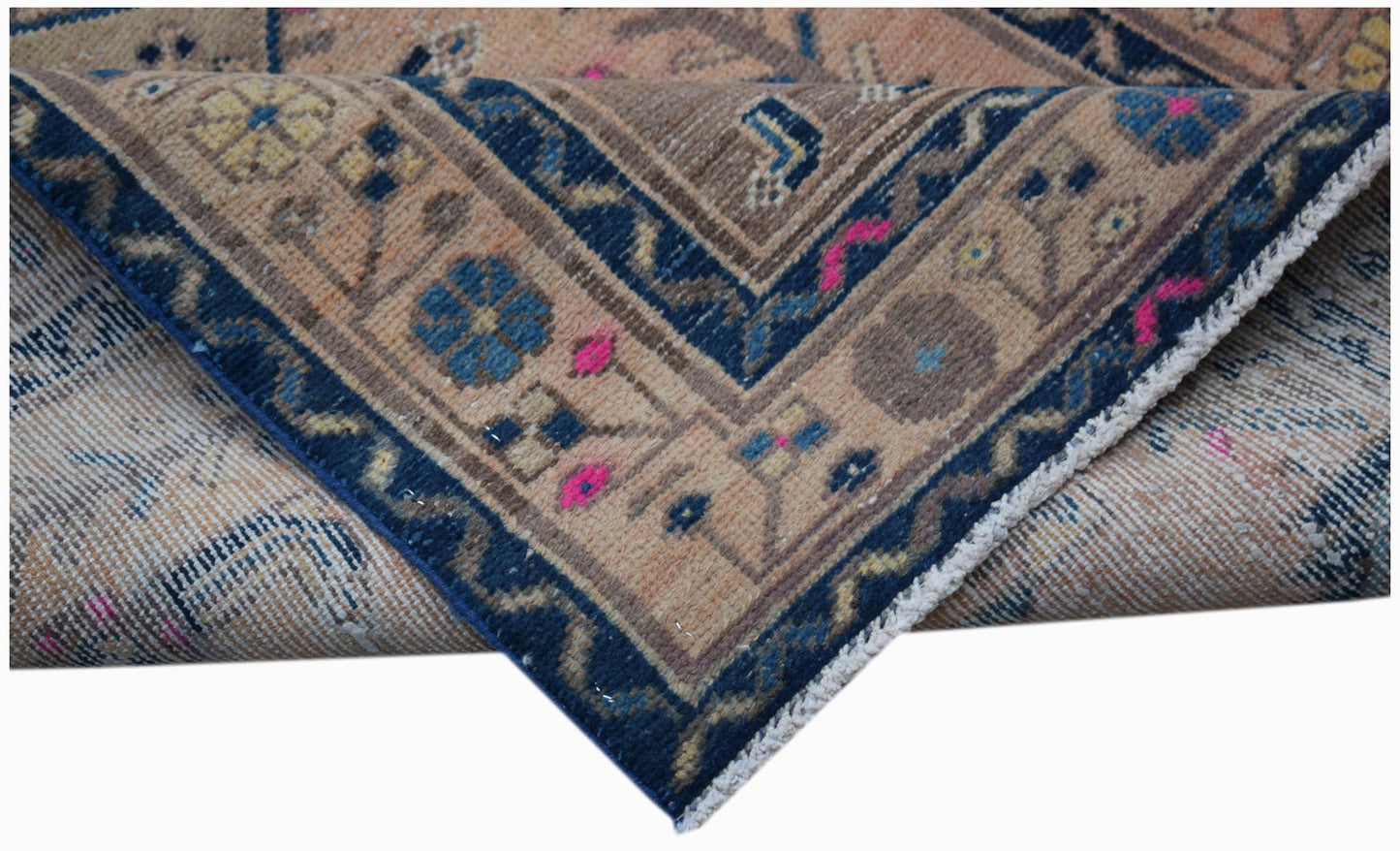 A folded vintage Persian rug featuring a blue border with floral patterns on a tan background.