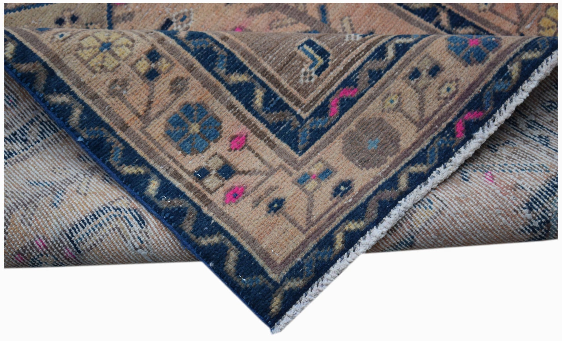 A folded vintage Persian rug featuring a blue border with floral patterns on a tan background.