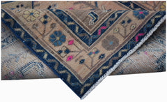 A folded vintage Persian rug featuring a blue border with floral patterns on a tan background.