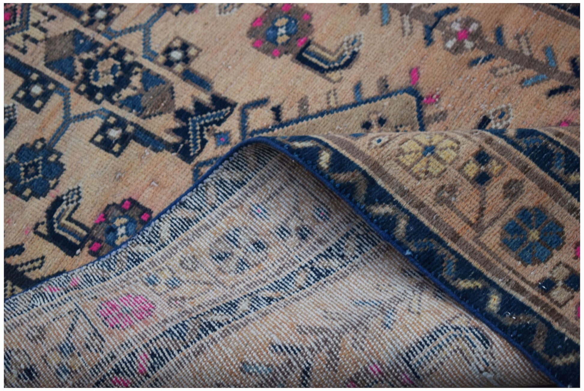 A vintage handwoven Persian rug with a worn, patterned design in shades of blue, pink, and tan.