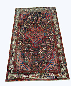 A vintage handmade Persian wool rug featuring a central medallion on a dark patterned field.