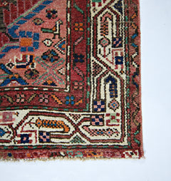 A vintage handmade Persian rug featuring intricate geometric patterns in red, blue, and cream.