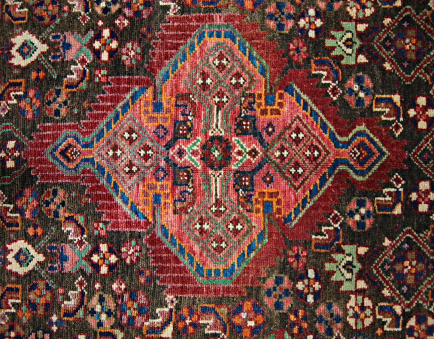 A vintage Persian rug featuring a central geometric medallion in red, blue, and green on dark wool.