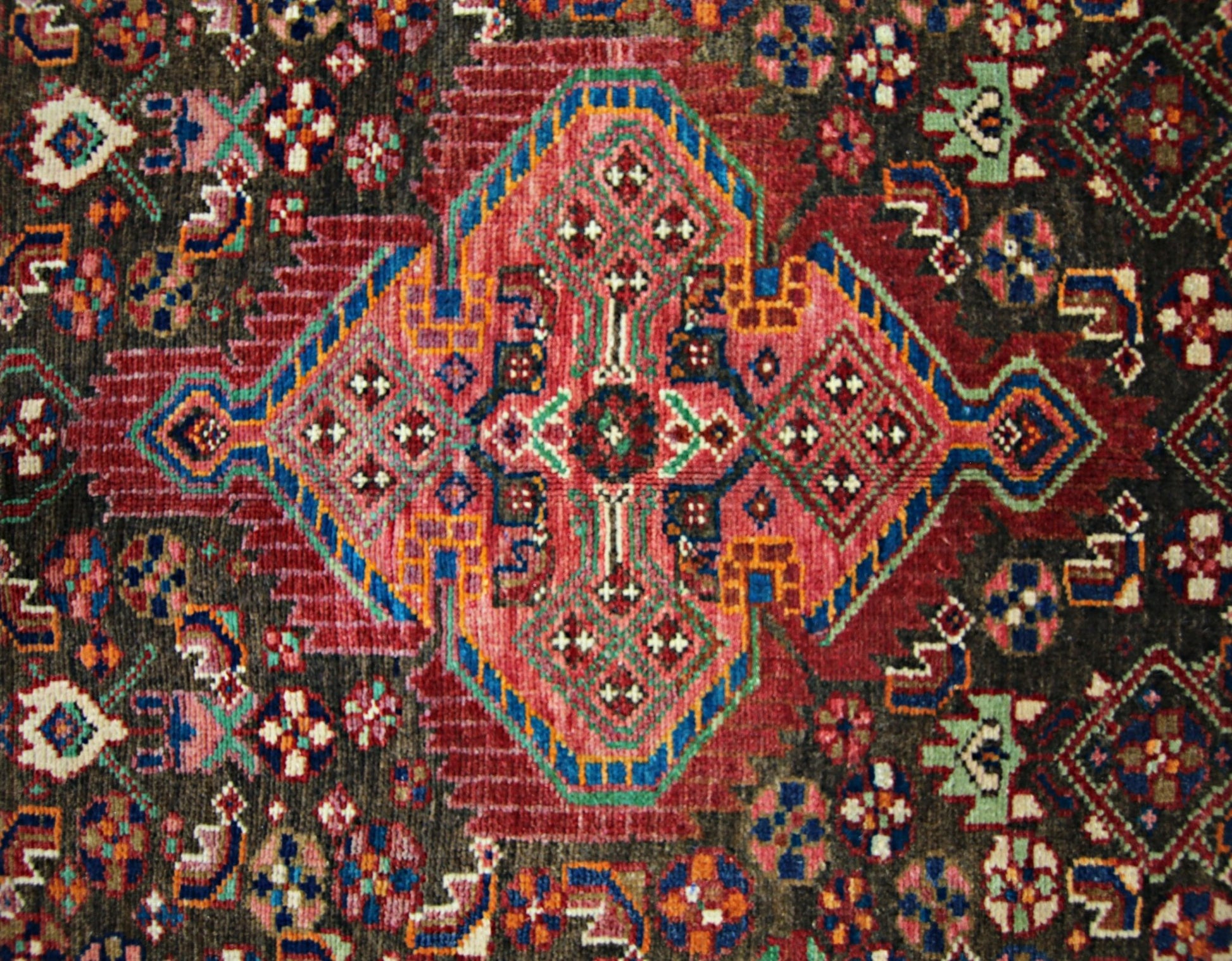 A vintage Persian rug featuring a central geometric medallion in red, blue, and green on dark wool.