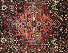 A vintage Persian rug featuring a central geometric medallion in red, blue, and green on dark wool.