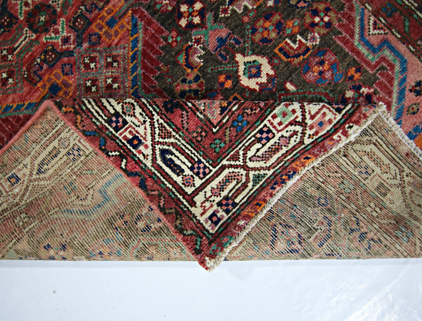 A vintage Persian rug with a folded corner revealing its intricate wool pile and cotton base.