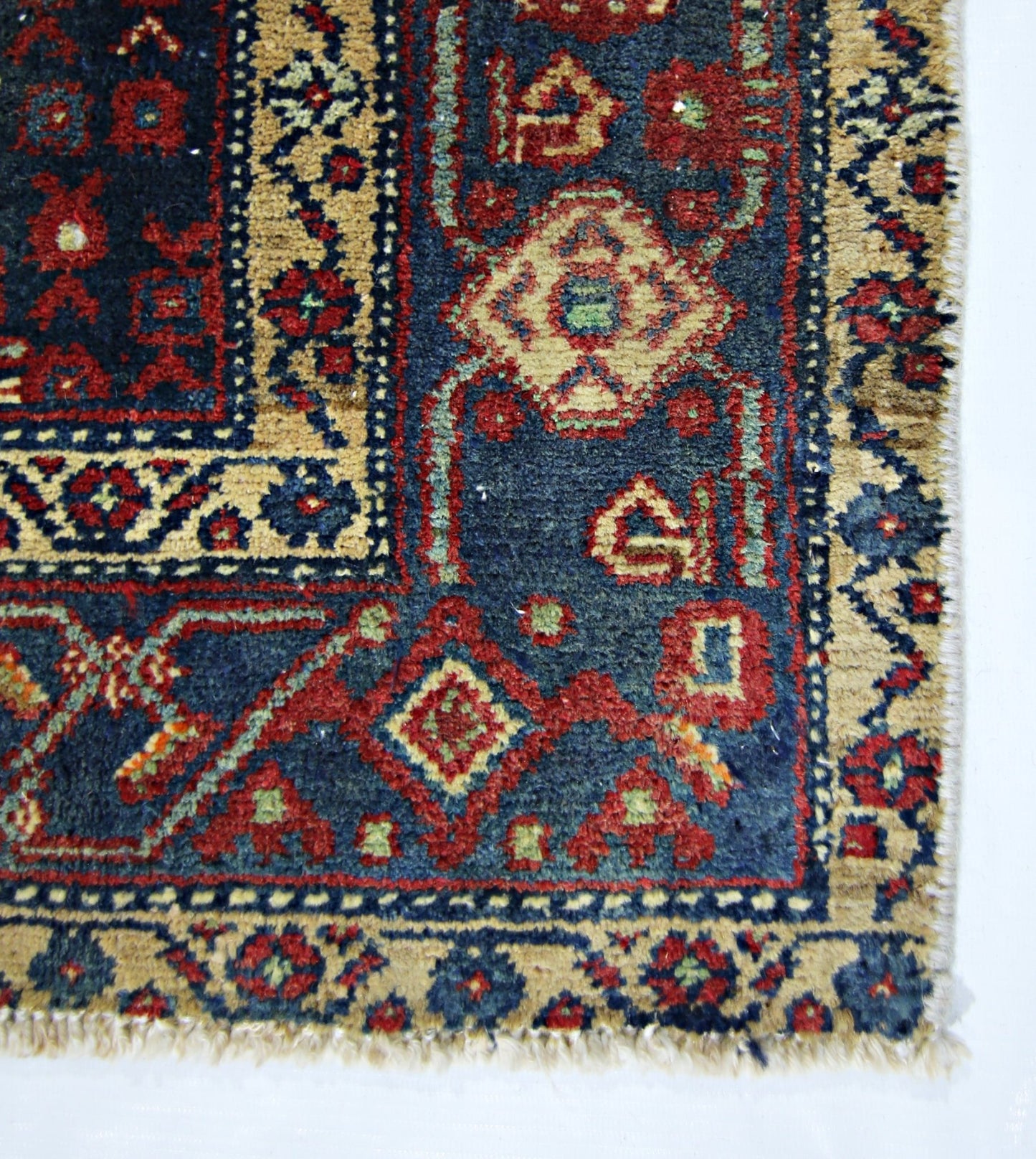 A vintage handmade Persian rug featuring intricate geometric patterns in red, blue, and tan.