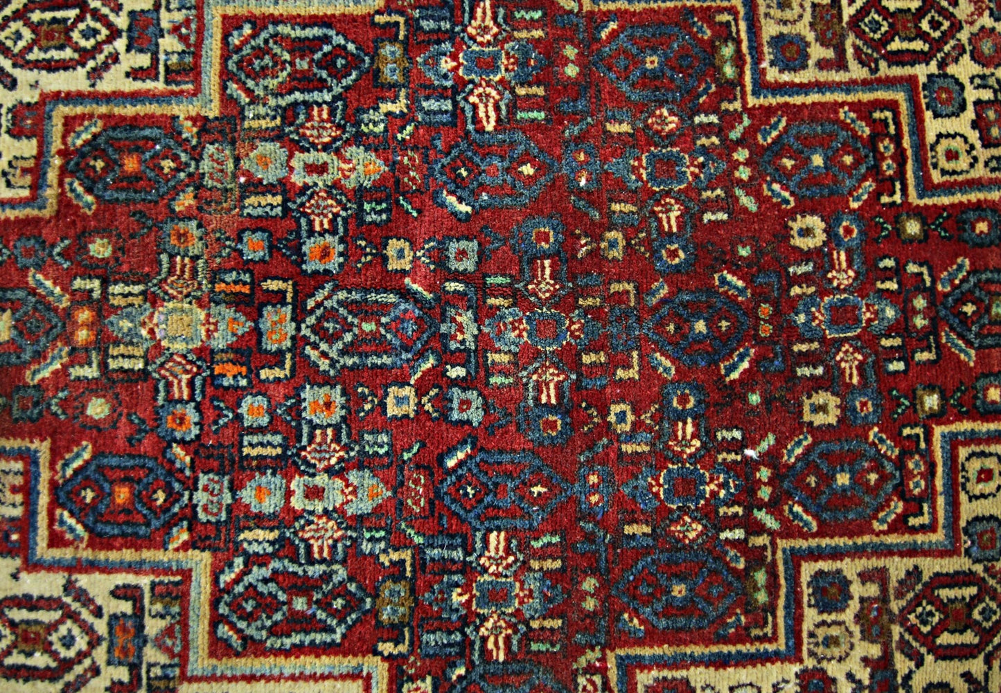 A vintage handmade Persian rug featuring an intricate geometric pattern in red, blue, and cream.