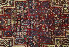 A vintage handmade Persian rug featuring an intricate geometric pattern in red, blue, and cream.