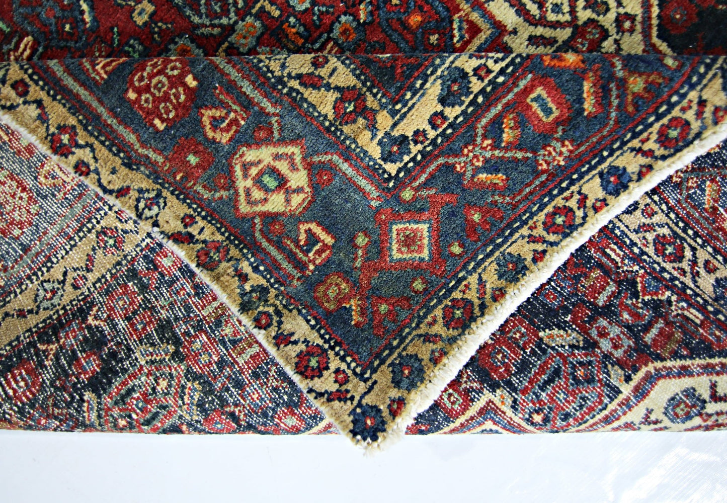 A folded vintage Persian rug featuring intricate geometric patterns in red, blue, and beige.