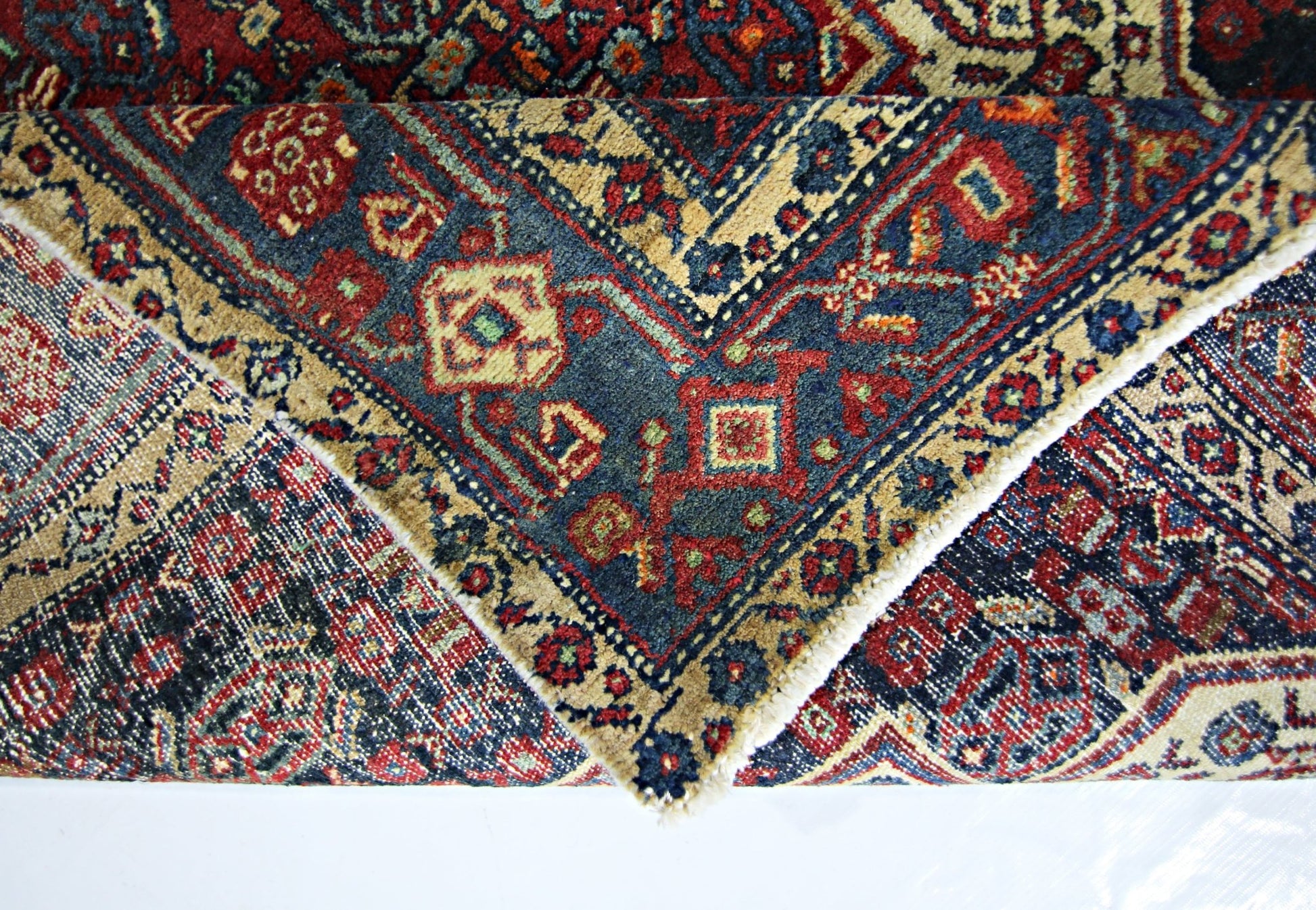 A folded vintage Persian rug featuring intricate geometric patterns in red, blue, and beige.