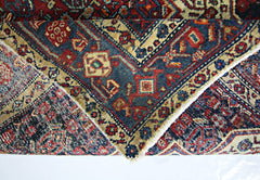 A folded vintage Persian rug featuring intricate geometric patterns in red, blue, and beige.