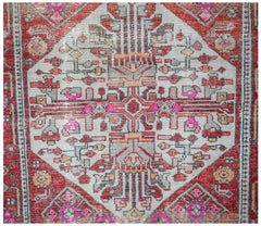 A handwoven vintage Persian rug featuring a geometric diamond medallion in red, grey, and pink.