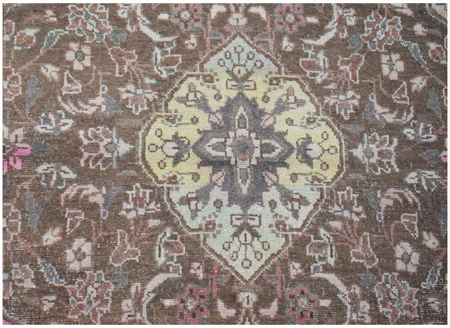A vintage handwoven Persian rug featuring a central yellow medallion on a brown floral field.