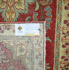 A vintage Persian rug with a red field and intricate floral patterns, shown with a product tag.