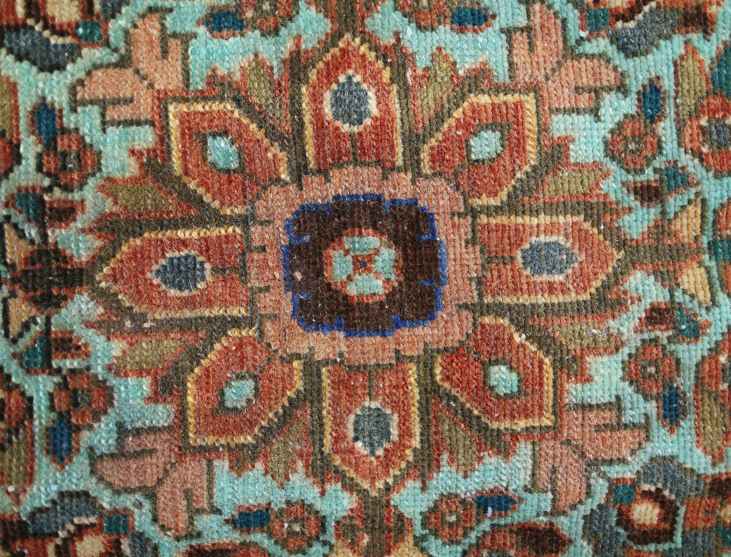 A close-up of a vintage Persian rug featuring a detailed floral medallion in rust and teal tones.
