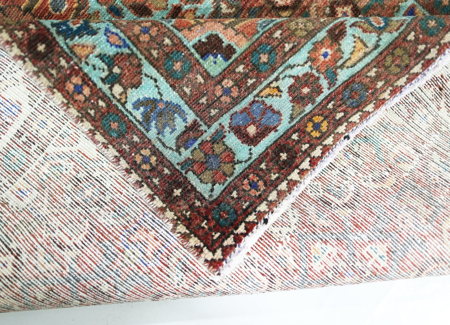 A corner of a vintage handmade Persian rug showing a detailed floral border in wool on cotton.