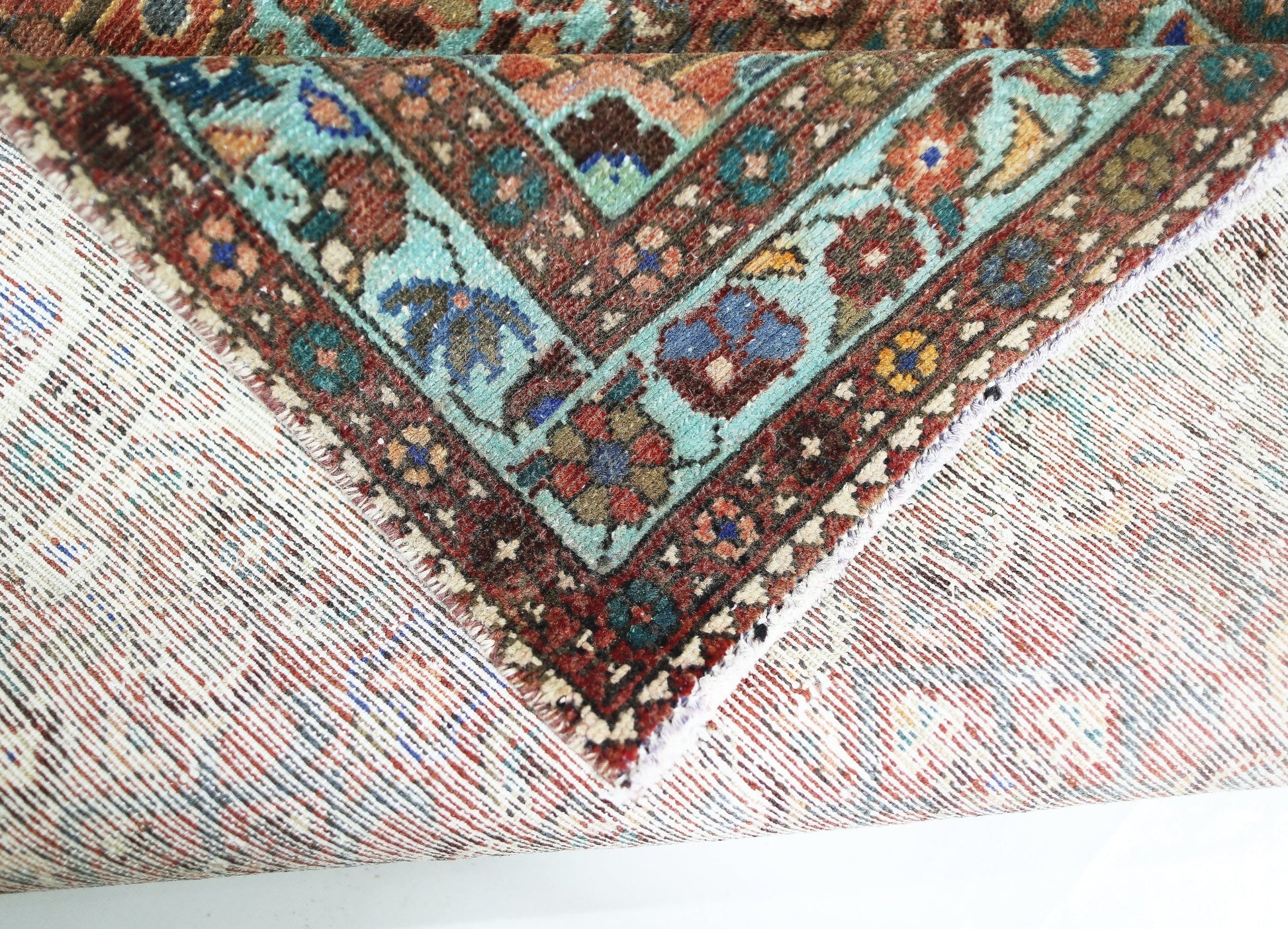A corner of a vintage handmade Persian rug showing a detailed floral border in wool on cotton.