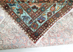 A corner of a vintage handmade Persian rug showing a detailed floral border in wool on cotton.