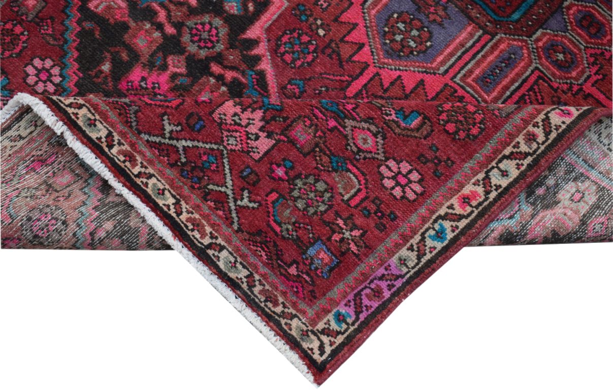 A folded vintage Persian wool rug featuring intricate tribal patterns in red, pink, and blue.