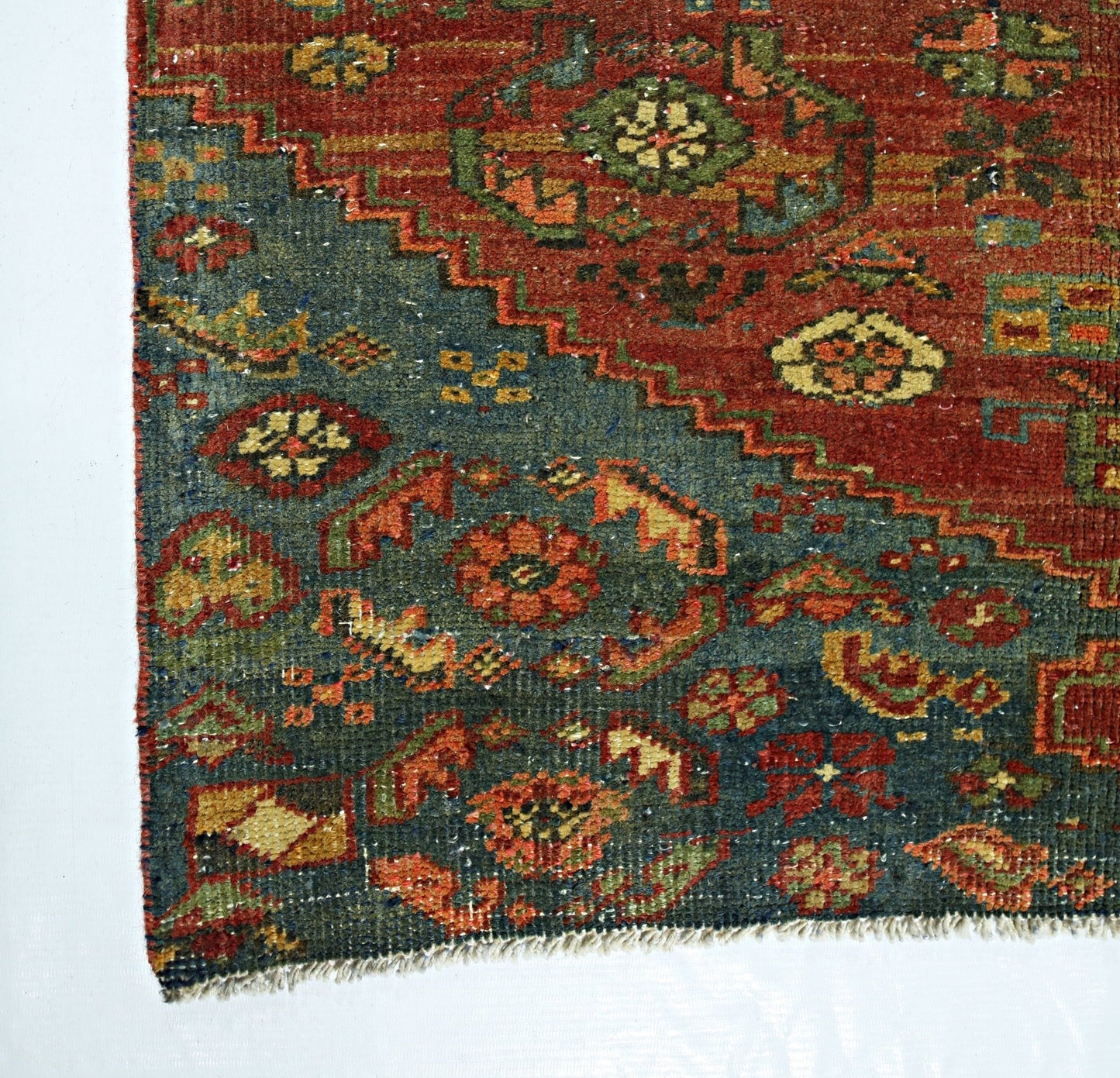 A vintage handmade Persian rug featuring a geometric floral pattern in red, blue, and green tones.