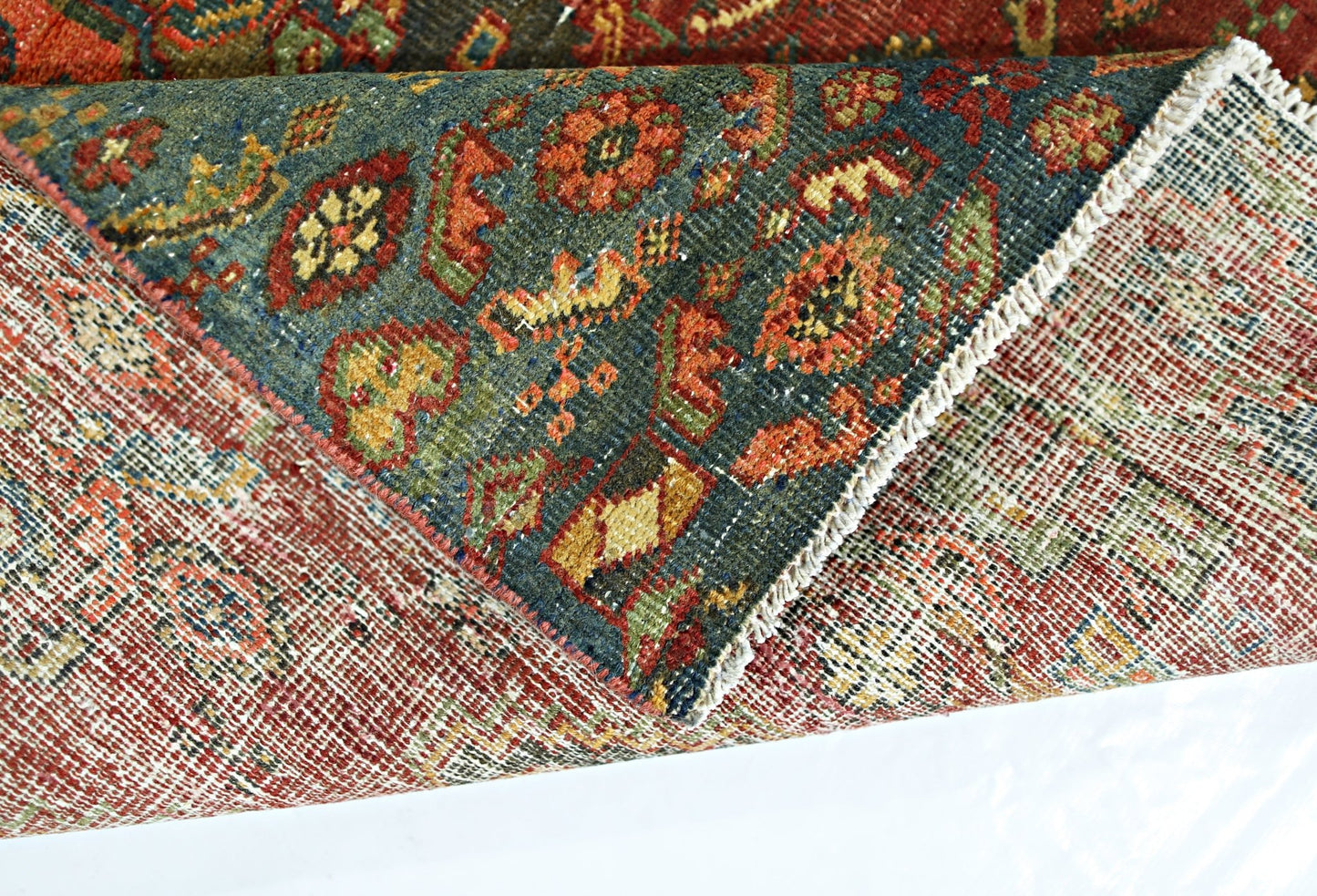 A folded vintage Persian rug featuring a dark blue field with intricate floral patterns in wool.